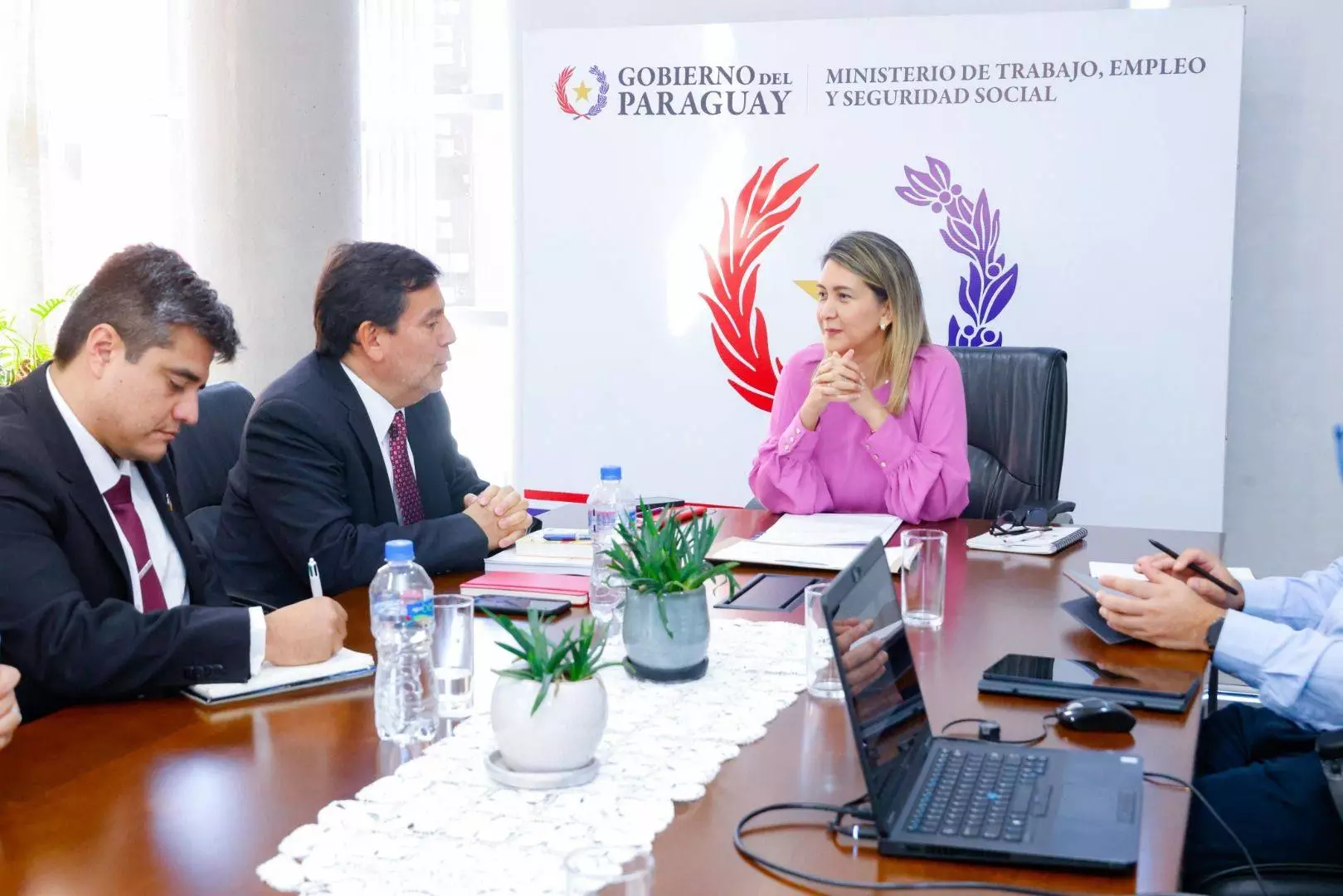 una mujer y dos varones sentados en una mesa conversando