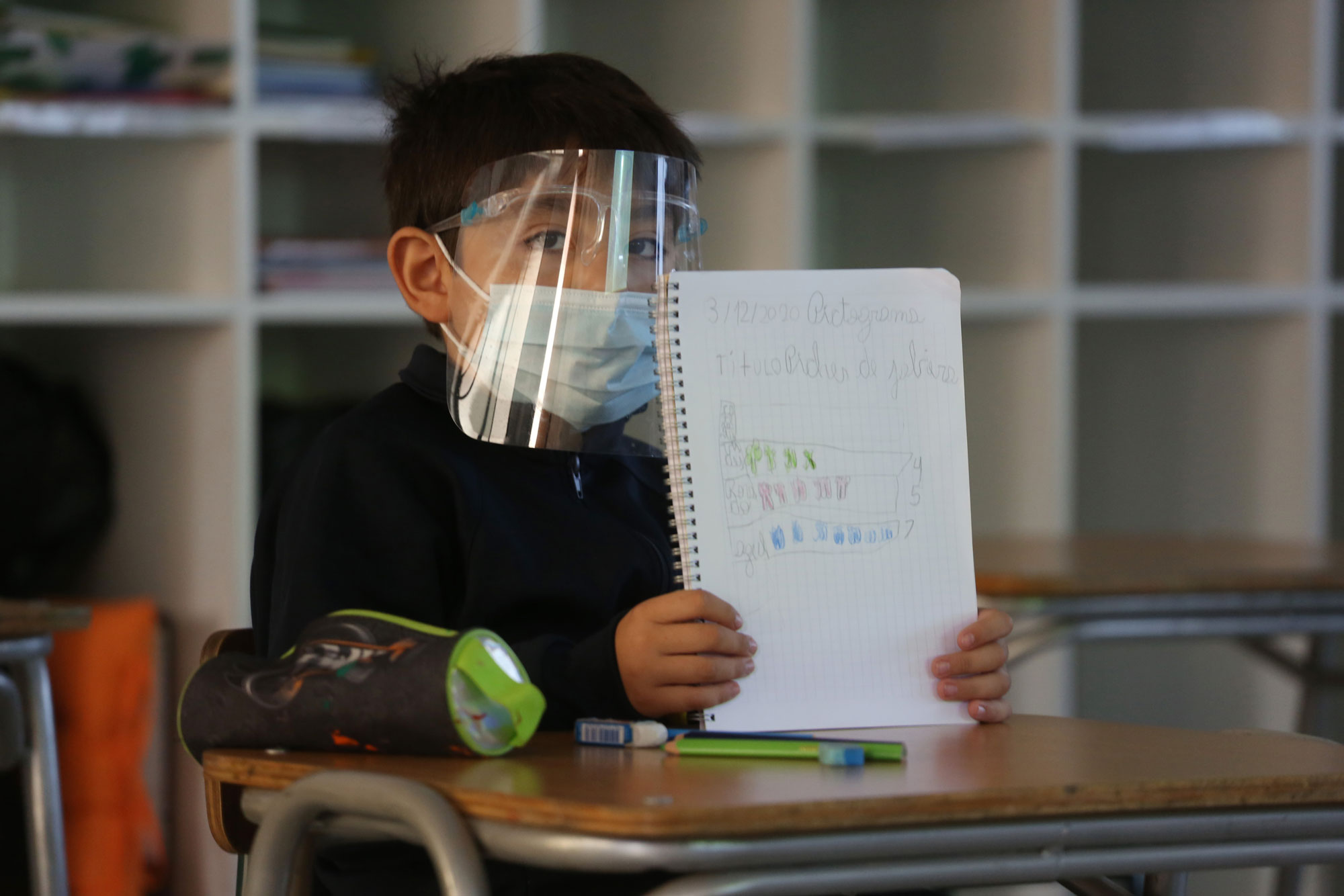 Niño en el colegio con mascarilla mostrando un cuaderno
