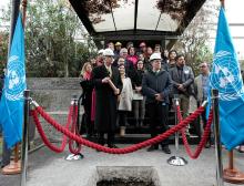 Secretario Ejecutivo con una cápsula de cobre en las manos y las banderas de las Naciones Unidas